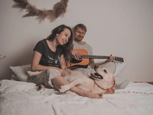 una pareja en una cama tocando guitarra a un perro