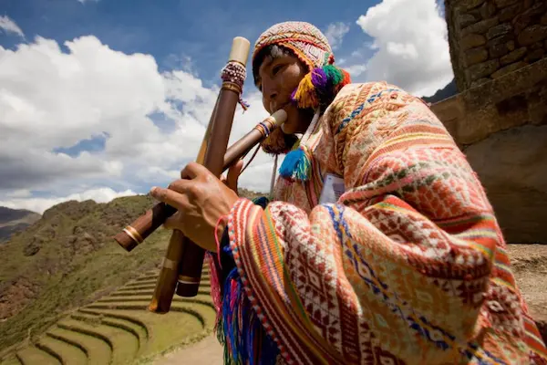 Hombre andino tocando un charango en medio de un paisaje montañoso, representando la instrumental andina.