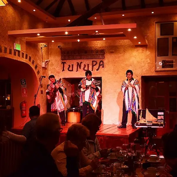 Escena panorámica de Cusco con músicos locales y turistas disfrutando de la música de cantantes peruanos.